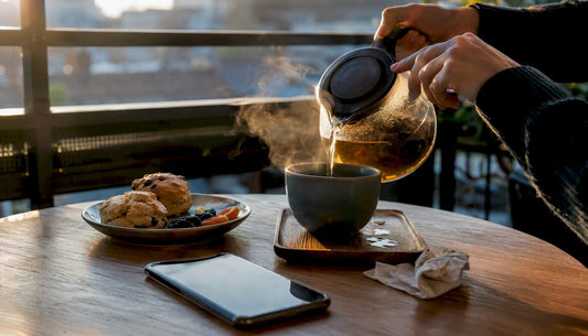 Hands pouring tea beside coffee cup and small plate